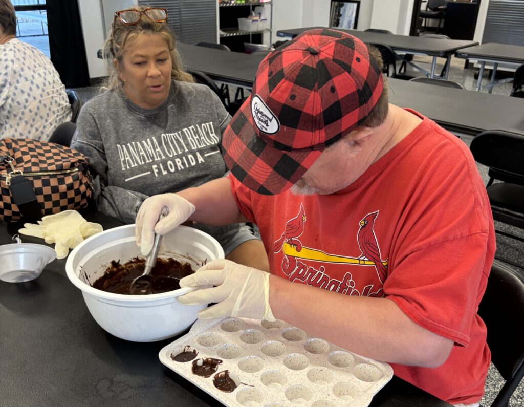 member spooning brownies into baking dish with volunteer looking on to help