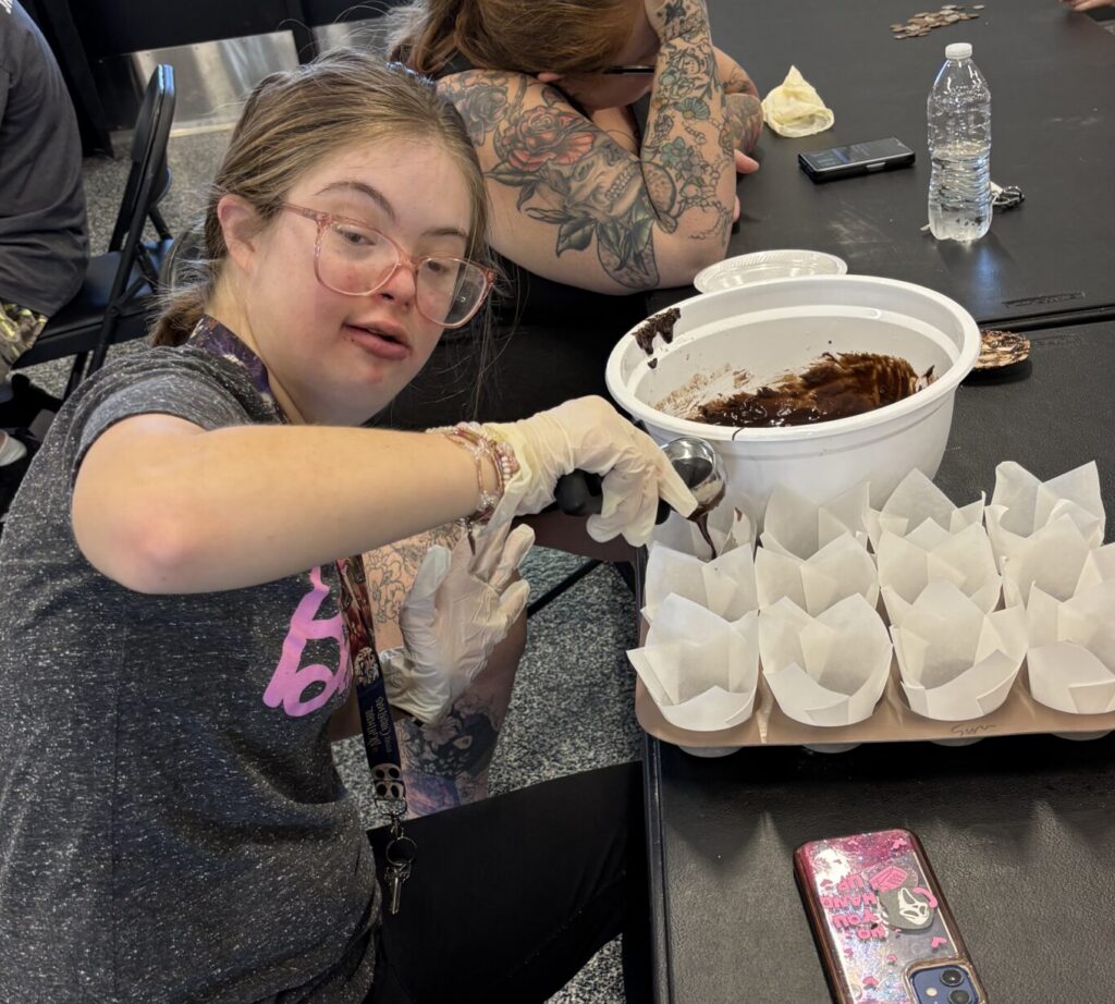member filling large muffin baking wrappers with brownie batter